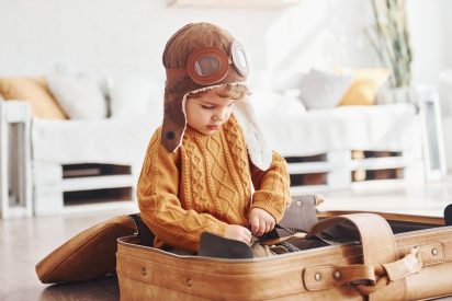little-boys-in-retro-pilot-costume-have-fun-and-sitting-in-suitcase-indoors-at-daytime.jpg